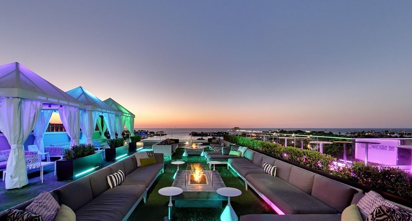 Rooftop lounge with fire pit and sofas overlooking the water at dusk