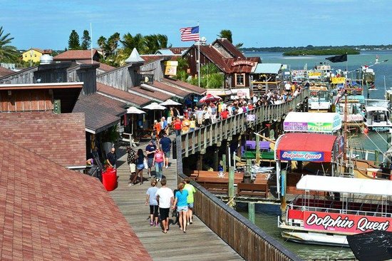 John's Pass Village boardwalk lined with shops, restaurants, boats, and an American flag